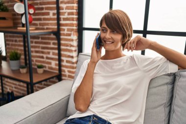 Evdeki kanepede oturmuş akıllı telefondan konuşan genç, güzel İspanyol kadın.