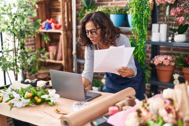Middle age woman florist using laptop reading document at flower shop