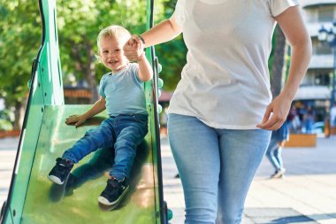 Anne ve oğlu parkta kayak yaparken kendinden emin bir şekilde gülümsüyor.