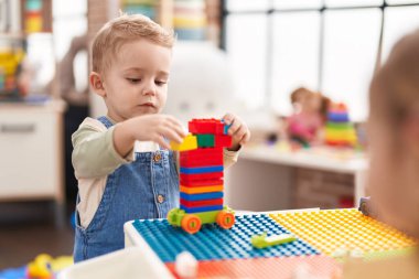 Adorable toddler playing with construction blocks standing at kindergarten