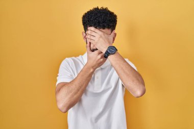 Sarı arka planda duran Arap adam gözleri ve ağzı elleriyle kapatıyor, şaşırmış ve şok olmuş. duygu gizleme 