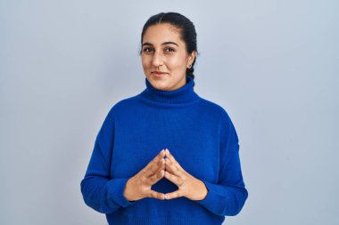 Young hispanic woman standing over isolated background hands together and fingers crossed smiling relaxed and cheerful. success and optimistic 