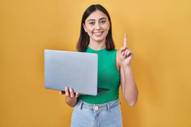 Hispanic girl working using computer laptop surprised with an idea or question pointing finger with happy face, number one 