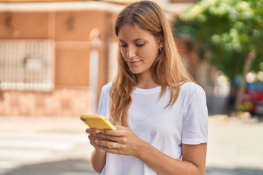 Young blonde girl smiling confident using smartphone at street
