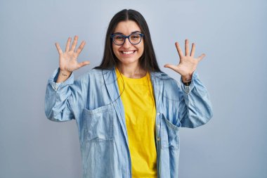 Mavi arka planda duran genç İspanyol kadın on numarayı gösterip işaret ederken kendinden emin ve mutlu bir şekilde gülümsüyor.. 