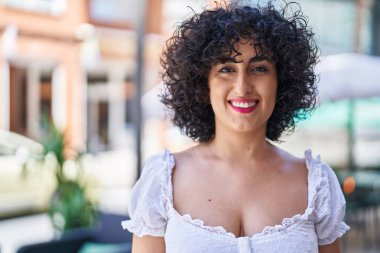 Orta Doğulu genç bir kadın sokakta kendine güvenerek gülümsüyor.