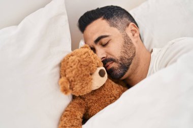 Genç İspanyol adam yatak odasında oyuncak ayıyla yatıyor.