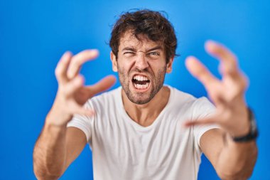 Mavi arka planda duran İspanyol genç adam öfkeyle bağırıyor, elleri boğazlamaya çalışıyor, deli gibi bağırıyor. 