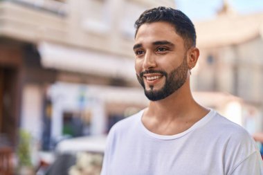 Genç Arap adam gülümsüyor. Kendinden emin. Caddenin kenarına bakıyor.