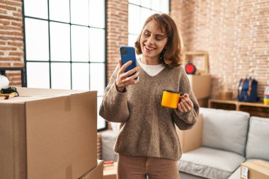 Young caucasian woman having video call drinking coffee at new home