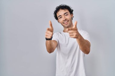 İzole edilmiş arka planda duran İspanyol adam mutlu ve komik yüzlü parmaklarını kameraya doğrultuyor. iyi enerji ve titreşimler. 