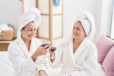 Mother and daughter wearing bathrobe drinking glass of wine at bedroom
