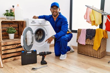 Çamaşır makinesi üzerinde çalışan genç Hintli teknisyen komik bir ifadeyle dilini dışarı çıkartıyor. duygu kavramı. 