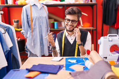 Young hispanic man tailor talking on smartphone at atelier