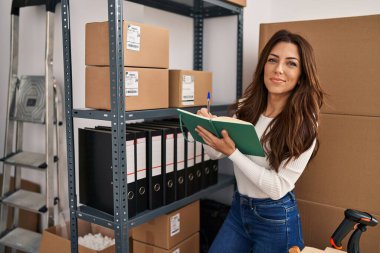 Genç İspanyol kadın ecommerce iş işçisi ofisteki kitap düzenleme paketleri üzerine yazıyor.