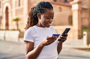 African american woman using smartphone and credit card at street