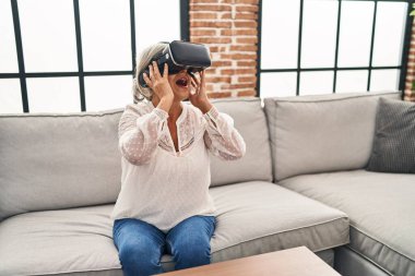 Evde sanal gerçeklik gözlüğü kullanan orta yaşlı bir kadın video oyunu oynuyor.