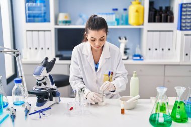 Young beautiful hispanic woman scientist mixing sample at laboratory