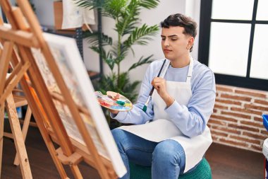 Young non binary man artist drawing with doubt expression at art studio