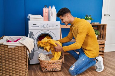 Genç İspanyol adam gülümsüyor çamaşırhanede çamaşır yıkıyor.