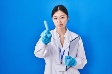 Laboratuvarda çalışan Çinli genç bir kadın parmağını kaldırmış ve kızgın bir ifadeyle işaret ediyor. 