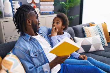Father and daughter reading book sitting on sofa at home