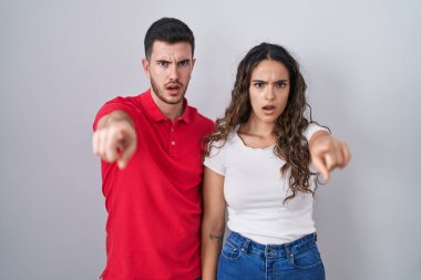 Young hispanic couple standing over isolated background pointing displeased and frustrated to the camera, angry and furious with you 