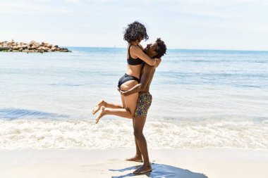 Plajda mayo giyen genç bir turist çifti sarılıyor..