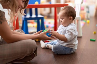 Anne ve oğlu anaokulunda yerde oturmuş toplarla oynuyorlar.