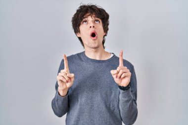 İzole edilmiş arka planda duran genç adam şaşırmış ve şaşırmıştı. Parmaklarıyla yukarı bakıyor ve kollarını kaldırıyordu.. 