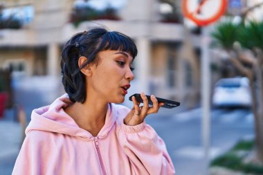 Gülümseyen genç bir kadın caddedeki akıllı telefondan konuşuyor.