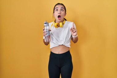 Spor kıyafetleri giyen genç Asyalı kadın şaşkınlık ve şaşkınlık içinde yukarı baktı ve parmaklarıyla işaret etti ve kollarını kaldırdı.. 