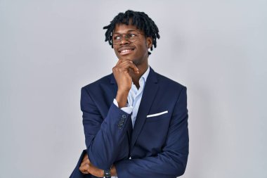 Young african man with dreadlocks wearing business jacket over white background with hand on chin thinking about question, pensive expression. smiling and thoughtful face. doubt concept. 