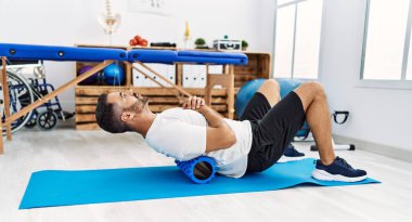 Genç İspanyol hasta gülümsüyor. Klinikte köpük silindir kullanarak rehabilitasyon seansına katılıyor.