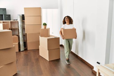 Orta yaşlı İspanyol kadın yeni evinde elinde karton kutuyla gülümsüyor.