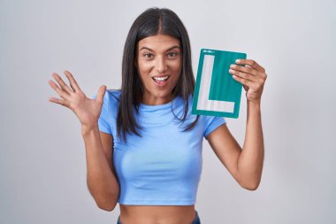 Brunette young woman holding l sign for new driver celebrating victory with happy smile and winner expression with raised hands 