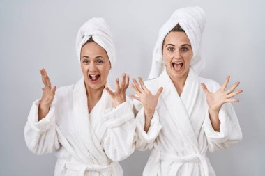 Middle age woman and daughter wearing white bathrobe and towel celebrating crazy and amazed for success with arms raised and open eyes screaming excited. winner concept 