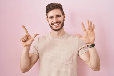 Pembe arka planda duran İspanyol sakallı adam yedi numaralı parmaklarını gösterip işaret ederken kendine güvenen ve mutlu bir şekilde gülümsüyor.. 