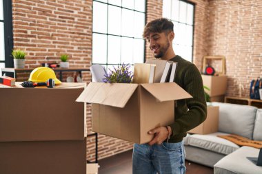 Young arab man smiling confident holding package at new home