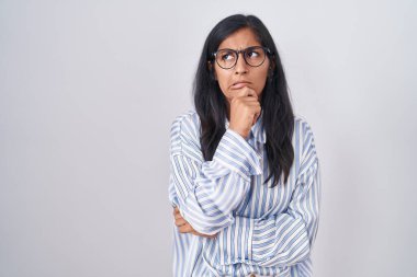 Young hispanic woman wearing glasses thinking worried about a question, concerned and nervous with hand on chin 