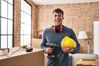 Young hispanic man working at home renovation winking looking at the camera with sexy expression, cheerful and happy face. 