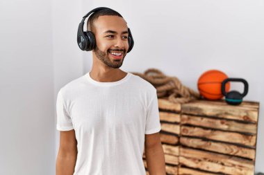 African american man listening to music using headphones at the gym looking away to side with smile on face, natural expression. laughing confident. 
