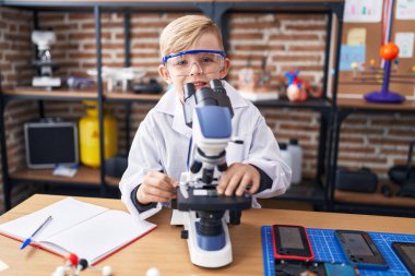 Adorable toddler student using microscope standing at classroom