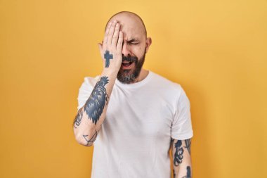 Sarı arka planda duran İspanyol dövmeli genç adam yarı yüzünü, göz ve ağzını eliyle kapatmaktan yorulmuş esniyor. Yüzüm acıyor.. 