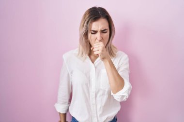 Pembe arka planda duran genç ve güzel bir kadın kendini iyi hissetmiyor ve soğuk algınlığının veya bronşitin belirtisi olarak öksürüyor. sağlık hizmeti kavramı. 