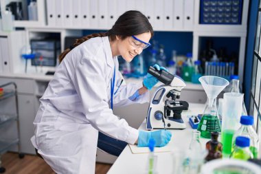 Genç bilim kadını laboratuarda mikroskop kullanarak deftere yazıyor.