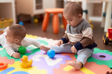 Anaokulunda yerde oturmuş hayalarıyla oynayan iki sevimli çocuk.