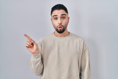 İzole edilmiş arka planda duran yakışıklı genç adam şaşırdı. Parmağını yana doğru gösterdi, ağzı açık hayret içinde kaldı.. 