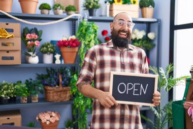 Young hispanic man with beard and tattoos working at florist holding open sign celebrating crazy and amazed for success with open eyes screaming excited. 