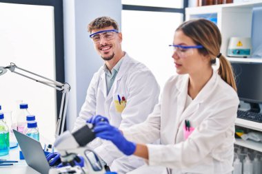 Genç erkek ve kadın bilim adamları laboratuarda mikroskop kullanıyorlar.